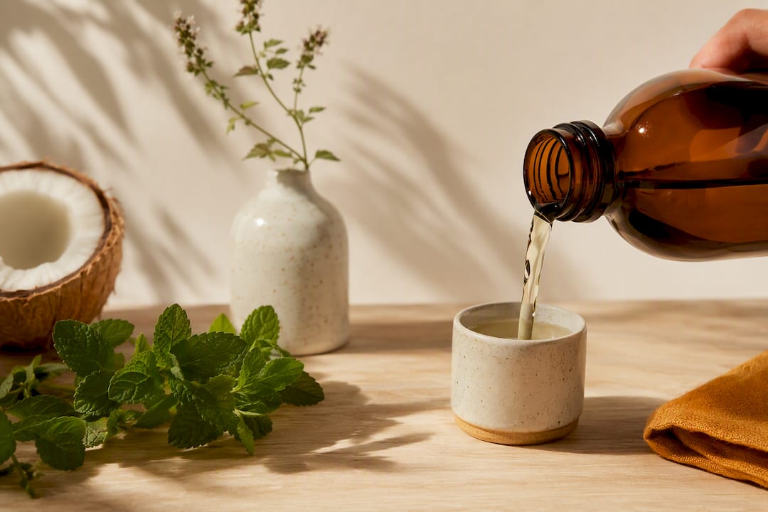 Natural mouthwash poured beside mint and coconut
